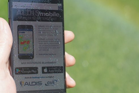 Smartphone mit ALDISmobile App und Regenbogen im Hintergrund